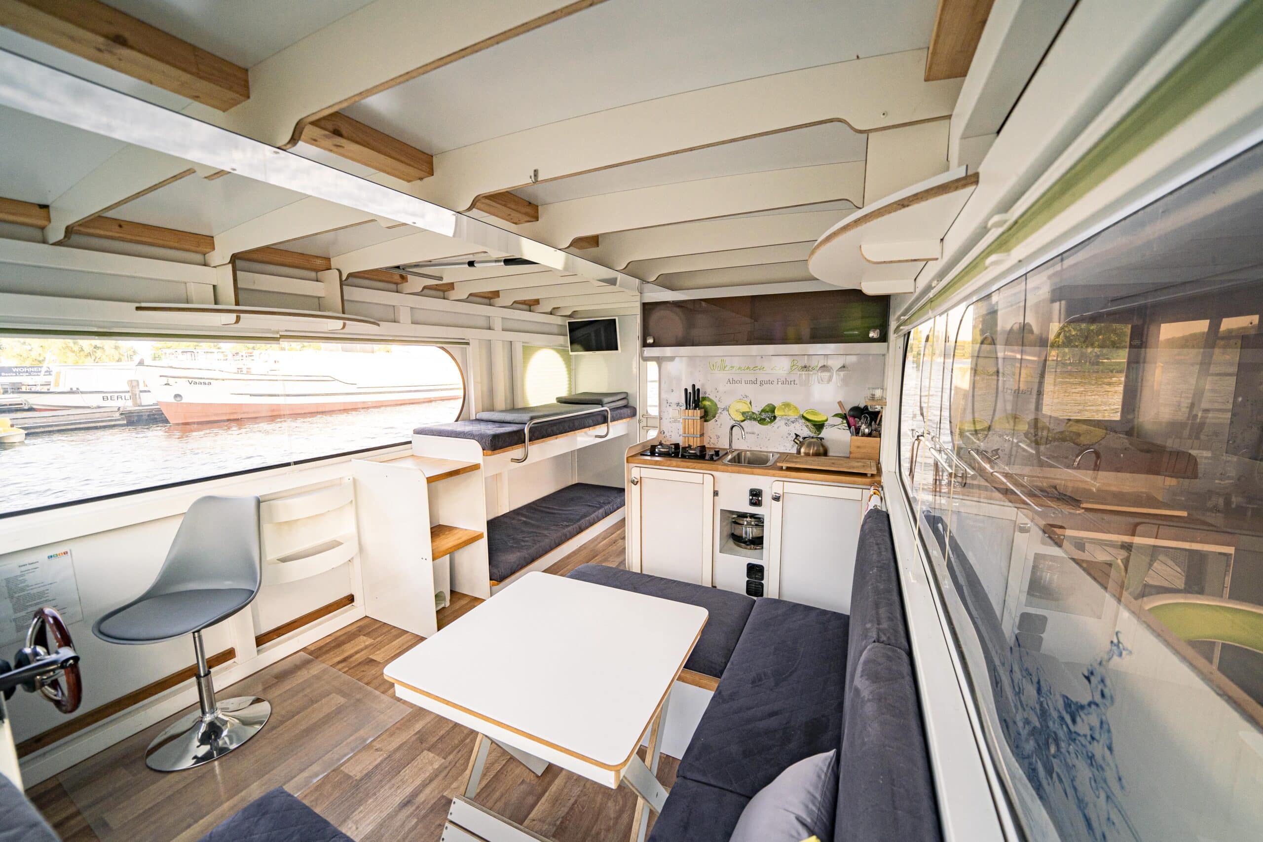 Adonis, COSY Hausboote, Innenraum ausgestattet mit Sofa, Tisch, Küche und Bettliegen